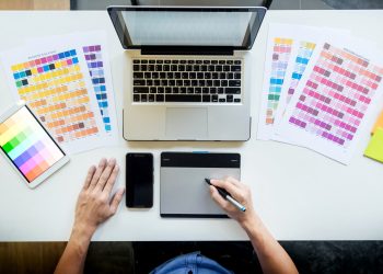 Top view of a young graphic designer working on a desktop computer and using some color swatches, top view.